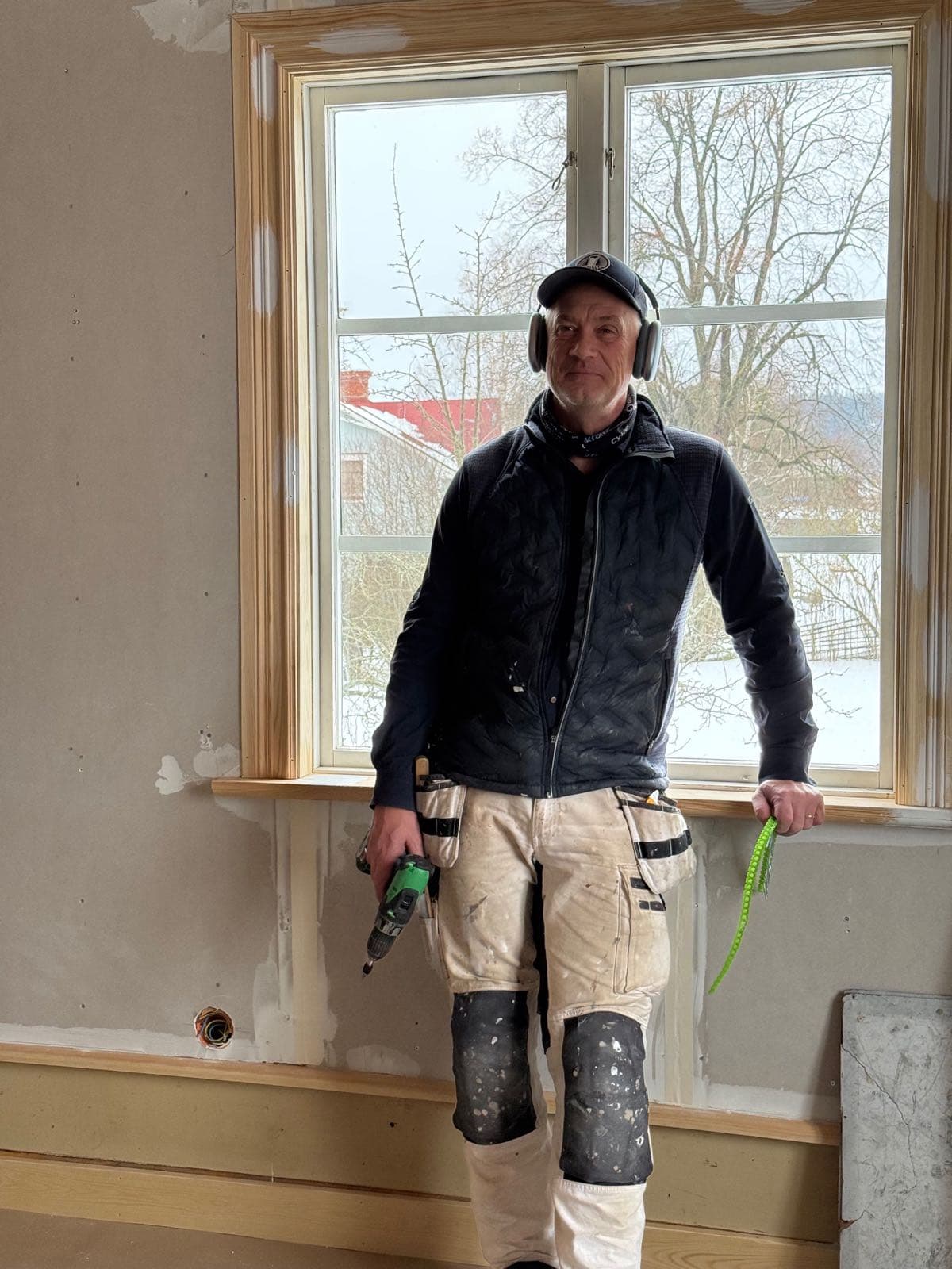 Målare med hörselkåpor vid ett spröjsat fönster i ett hus under renovering