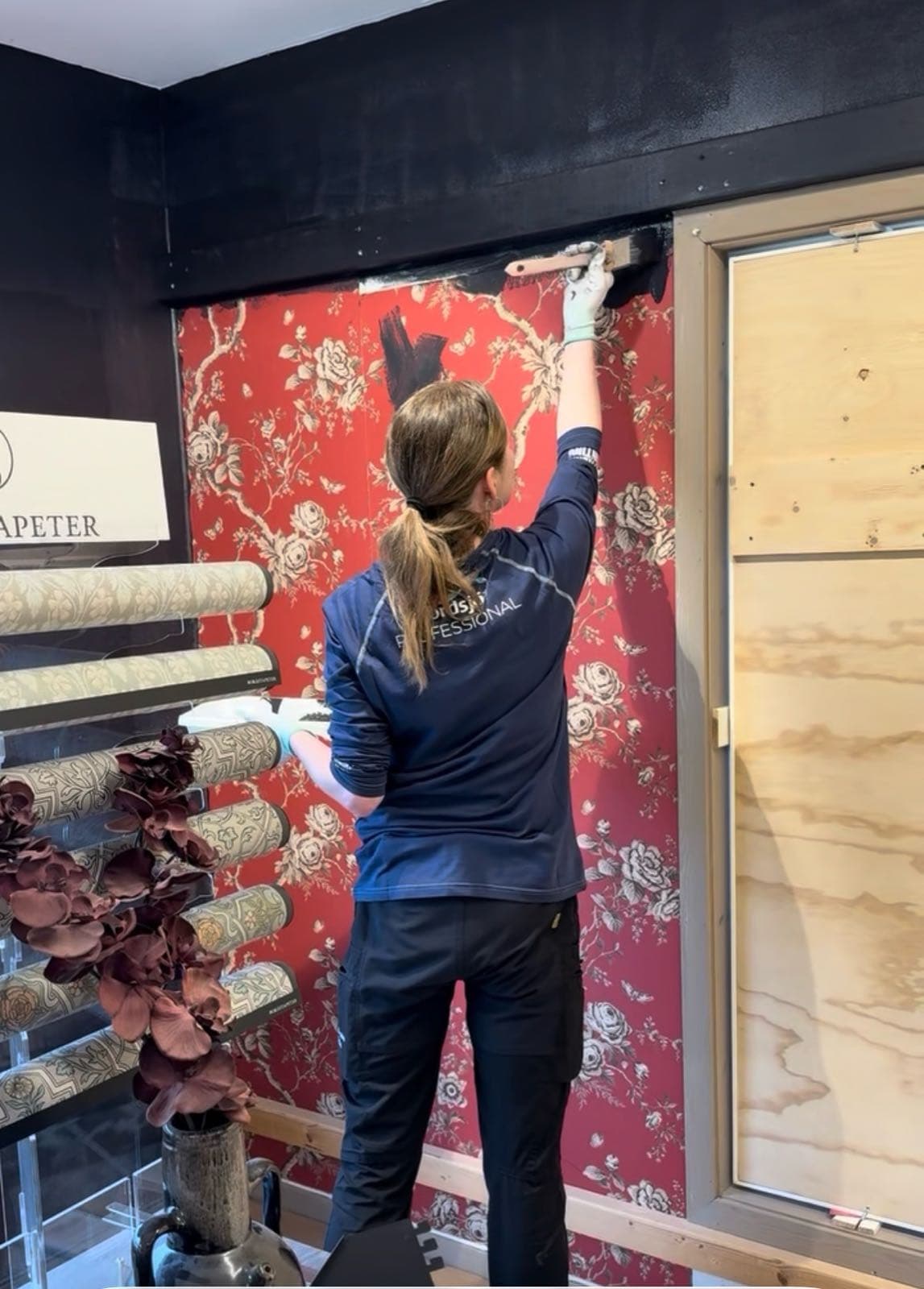 Medarbetare sätter upp en röd blommig tapet på butikens provvägg